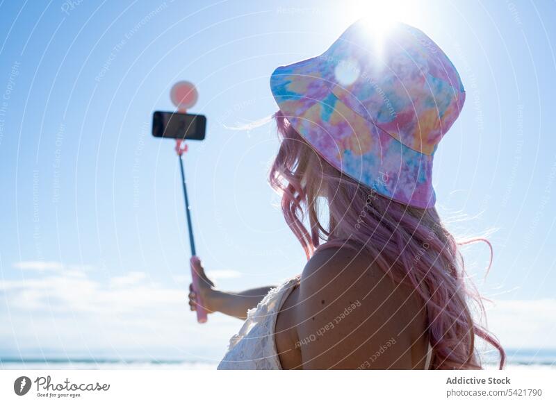 Anonymous woman with pink hair taking selfie on beach summer selfie stick smartphone self portrait seashore cheerful having fun female take photo smile gadget