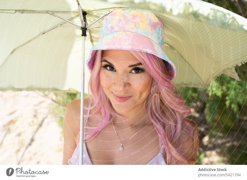 Content woman under umbrella on beach in summer looking at camera vacation seashore summertime enjoy hide sunny female happy cheerful smile positive freedom