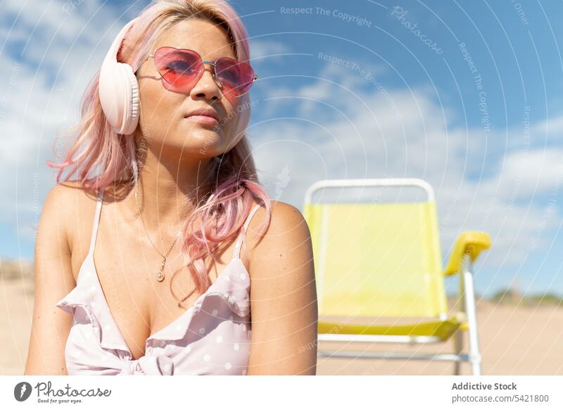 Woman listening to music on beach in summer woman headphones carefree chill summertime seaside female pink hair relax enjoy calm content tranquil rest serene