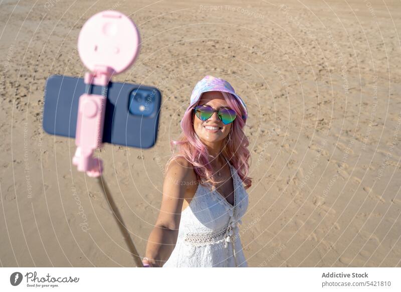 Smiling woman with pink hair taking selfie on beach summer selfie stick smartphone self portrait seashore cheerful having fun female take photo smile gadget