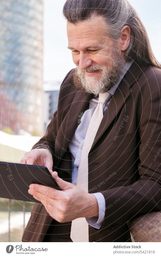 Mature bearded businessman using tablet on street gadget digital urban formal communicate online browsing device positive surfing internet male middle age