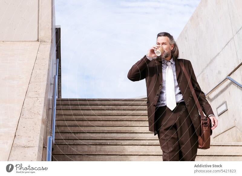 Stylish businessman with takeaway coffee on stairway in city step classy confident elegant style drink middle age mature gray hair to go disposable male