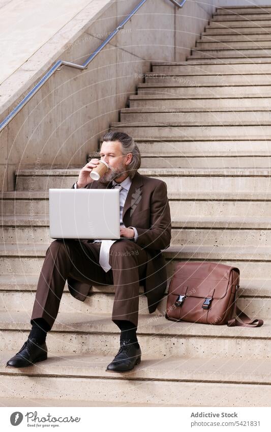 Mature man in suit using laptop on stairs businessman online remote style happy gadget internet communicate entrepreneur positive smile middle age mature aged