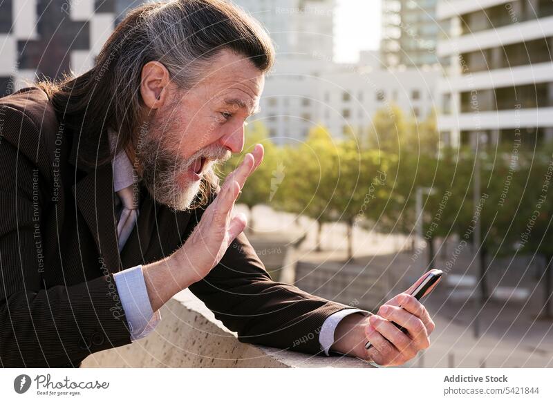 Happy bearded businessman on a video call on mobile phone in city smartphone talk urban smile communicate style happy modern mature middle age gray hair elegant