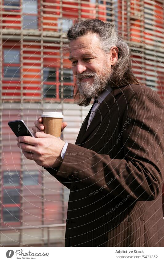 Aged businessman with coffee using smartphone gadget takeaway cup smile beard modern mature middle age executive gray hair browsing message drink communicate