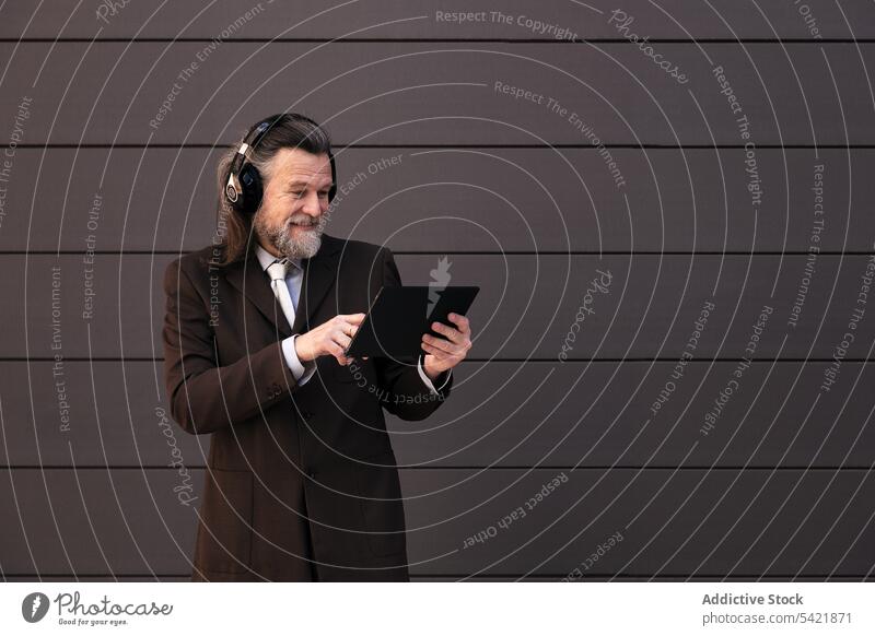 Happy mature businessman with headphones and tablet digital online communicate listen gadget using happy style middle age gray hair beard aged device internet