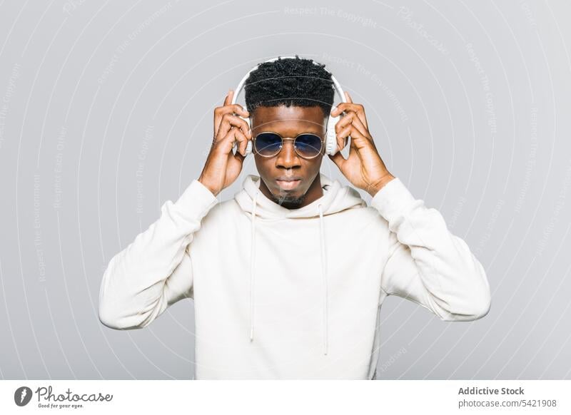 Cheerful black man in trendy outfit listening to music headphones style hipster white sunglasses hoodie fashion young african american ethnic modern male happy