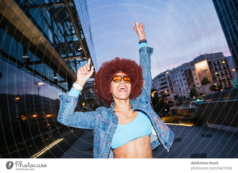 Stylish woman having fun on dark street afro style fashion outfit building urban evening happy apparel positive smile arms raised carefree glee optimist slender