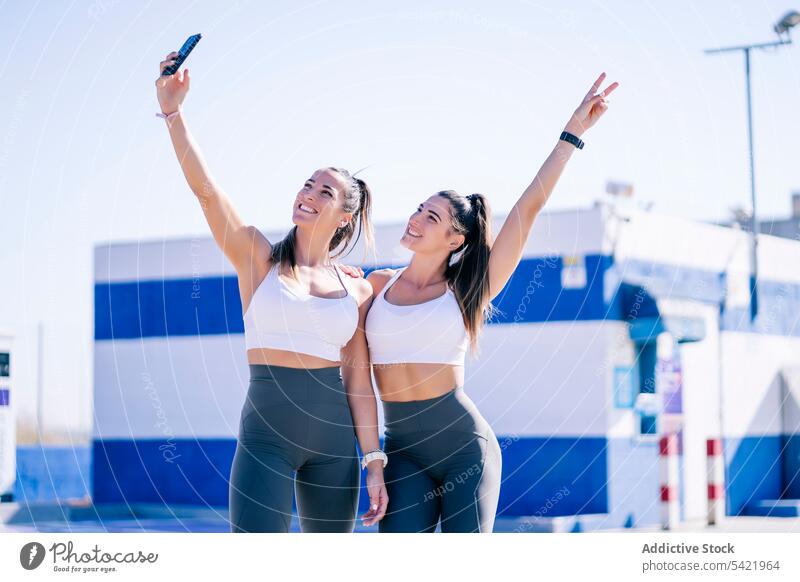 Cheerful twin sisters taking selfie on sport ground women cheerful smartphone fit using sporty together self portrait cellphone lifestyle stand female slim