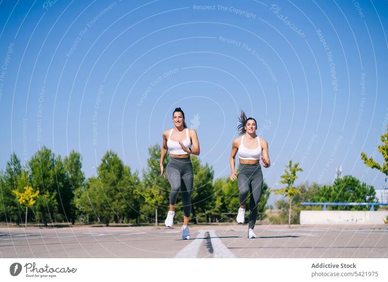 Content twin sisters jogging on asphalt women run fit fitness activity sporty together lifestyle female slim sibling wellbeing lady smile sportswear