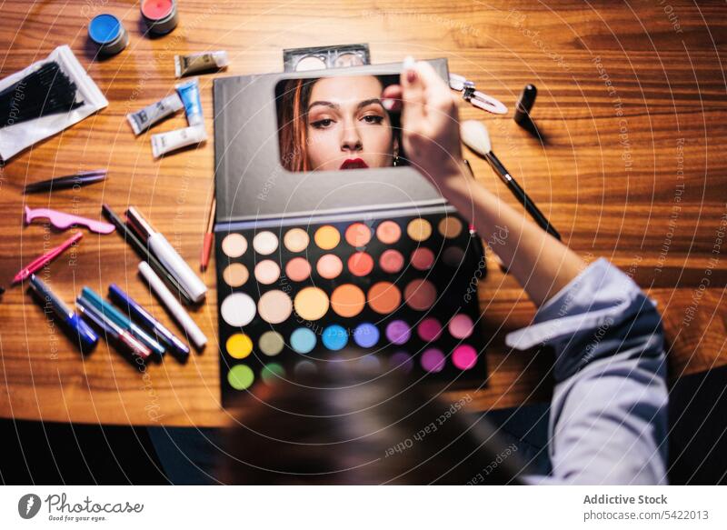 Non binary looking into mirror at table with cosmetics non binary transgender lgbtq makeup visage eyeshadow red lips set beauty product daily feminine light