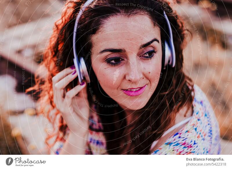 portrait outdoors of a young beautiful woman at sunset listening music on headset and smiling. Lifestyle and music concept casual fun young adult app