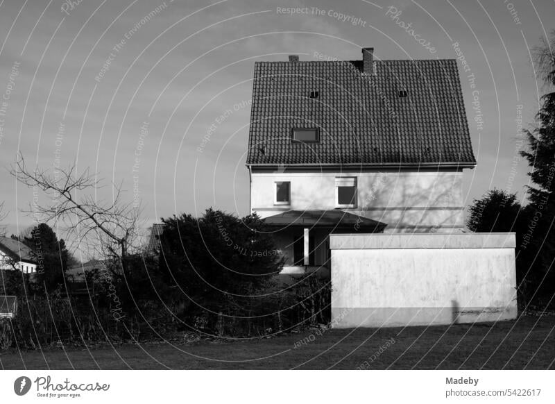 Old residential house with garage and large tiled roof against the sky in sunshine in Oerlinghausen near Bielefeld on the Hermannsweg in the Teutoburg Forest in East Westphalia-Lippe in neo-realistic black and white