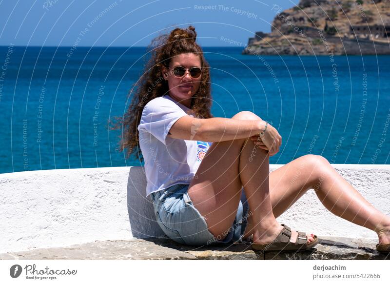 Young lady with sunglasses leans casually against a small wall. Behind her the blue sea of Crete. Lady Exterior shot Feminine Colour photo Adults Lifestyle