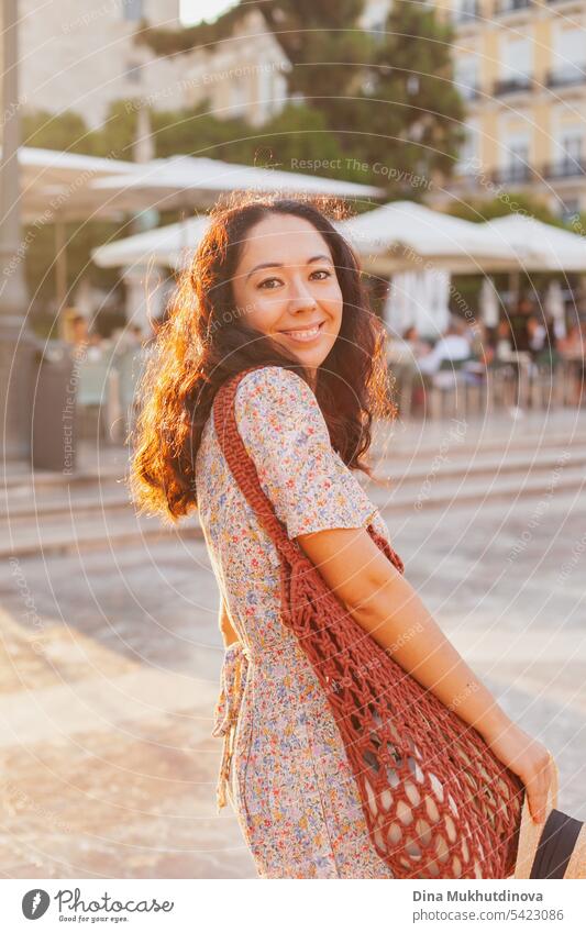 beautiful brunette woman tourist in European city smiling at sunset, walking on the street near cafe or restaurant terrace. Female solo traveler looking to the camera in Valencia, Spain.