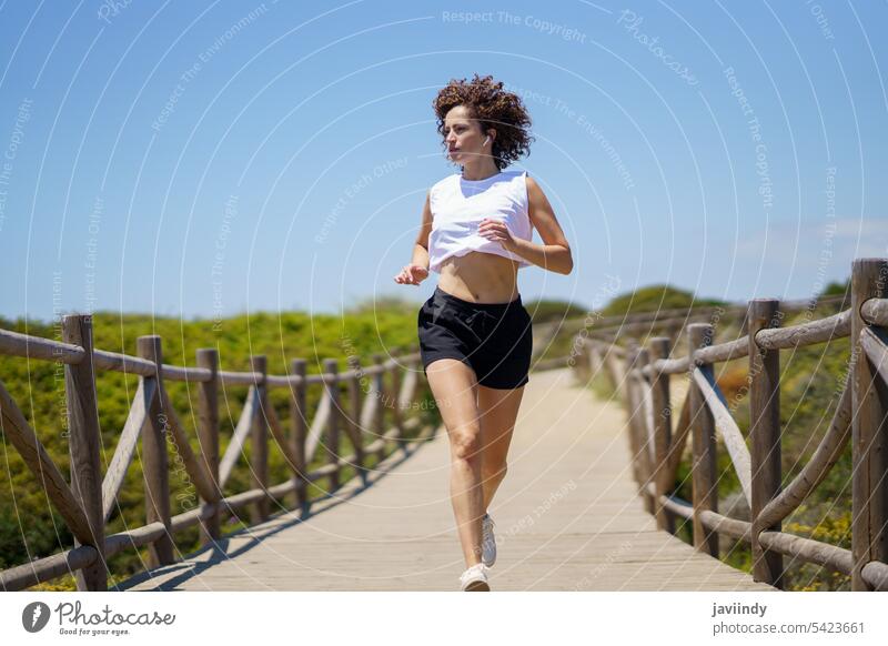 Sportswoman running along wooden path on sunny day sportswoman jog fitness warm up exercise workout athlete boardwalk training jogger wellbeing activity healthy