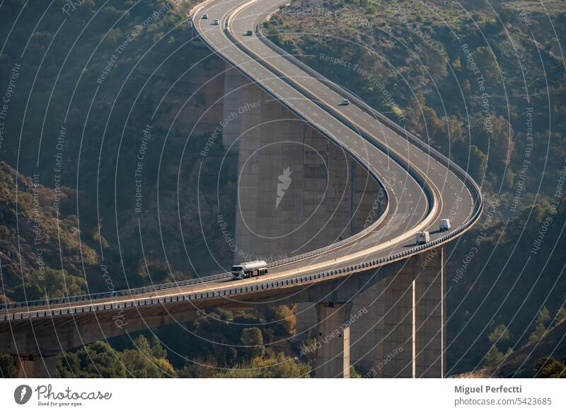 Huge viaduct crossing a ravine with a fuel tanker truck and several vehicles circulating on the road, elevated view. highway curve engineering tank truck