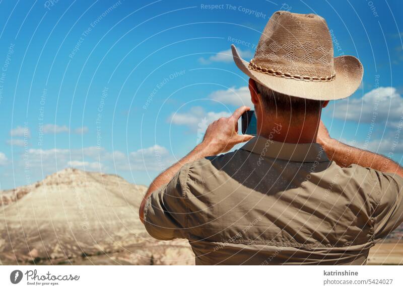 Man with shirt and cowboy hat taking photos with mobile phone during trekking in mountains man hiking nature outdoor walking acivity back view close up Travel