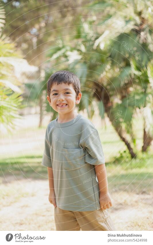 diverse kid standing in the park, smiling and looking to the camera. Five or six years old boy in the park in summer with palm trees as background. child