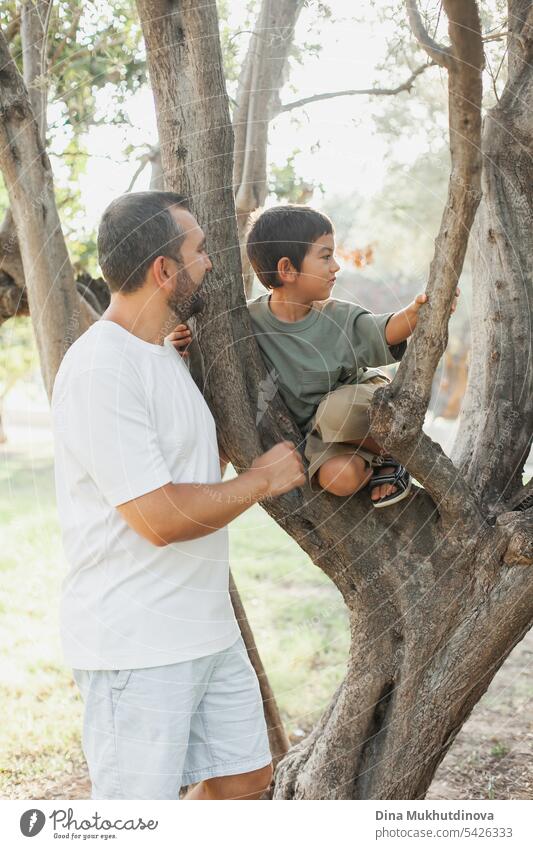 Father's Day. Dad with son in summer park climbing tree, having fun. Happy childhood activity. Father and son bonding, quality time together. Man Boy (child)