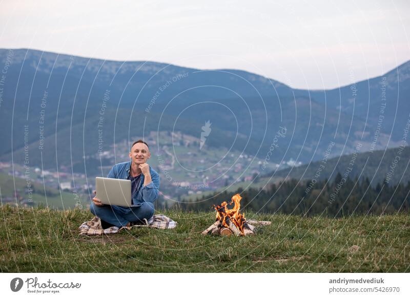 Man working outdoors with laptop sitting in mountains. Concept of remote work or freelancer lifestyle. Cellular network broadband coverage. internet 5G. Hiker tourist enjoying valley view