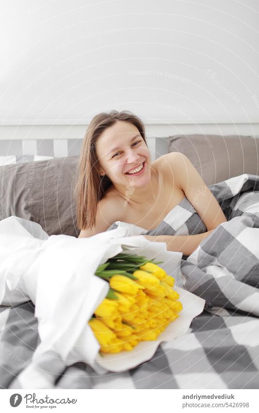 happy Girl with flowers yellow tulips lying on a bed with enjoying flowers and romantic gift in Valentine day. She just woken up and have presented her a bouquet of flowers. A birthday, woman's day,