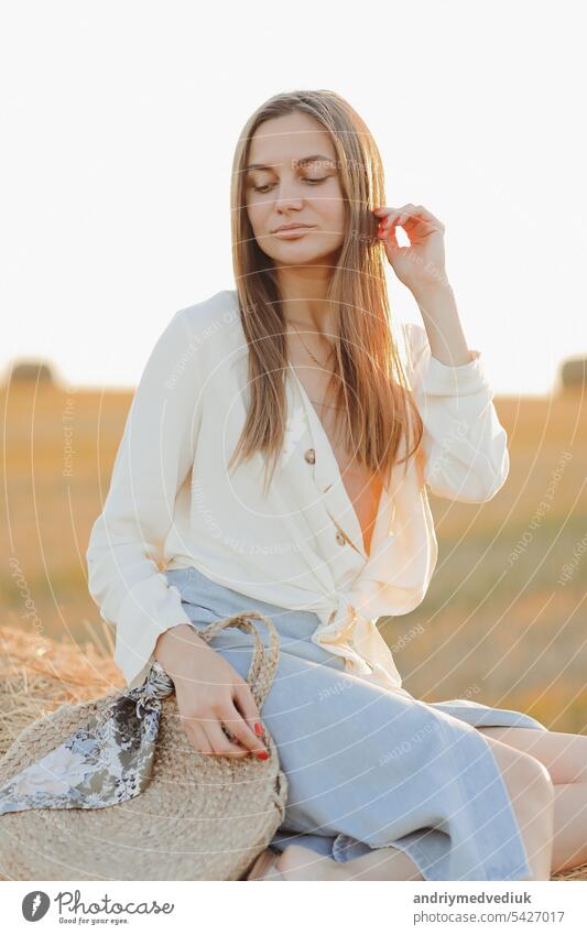 Beautiful portrait of a young woman during the sunset with warm yellow sun rays on her face with bales of straw on the background rural beautiful countryside