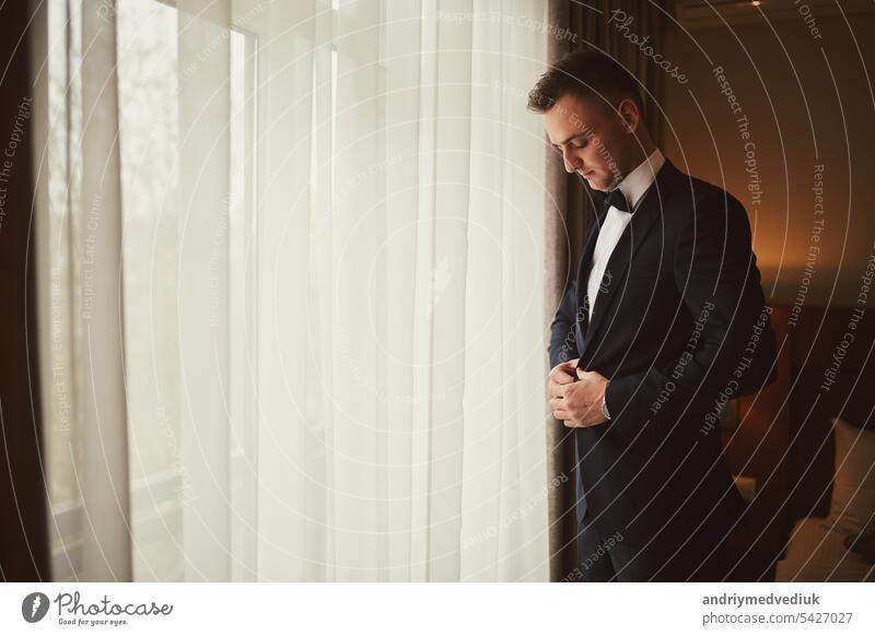 Morning of the groom before the wedding. Groom morning preparation. Young and handsome groom getting dressed in a wedding suit. tie background people person
