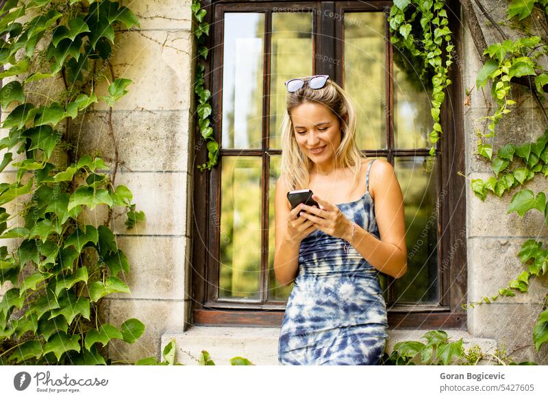 Pretty young woman using mobile phone by the old house with ivy happy beautiful cellphone female pretty people lifestyle smartphone summer smile attractive
