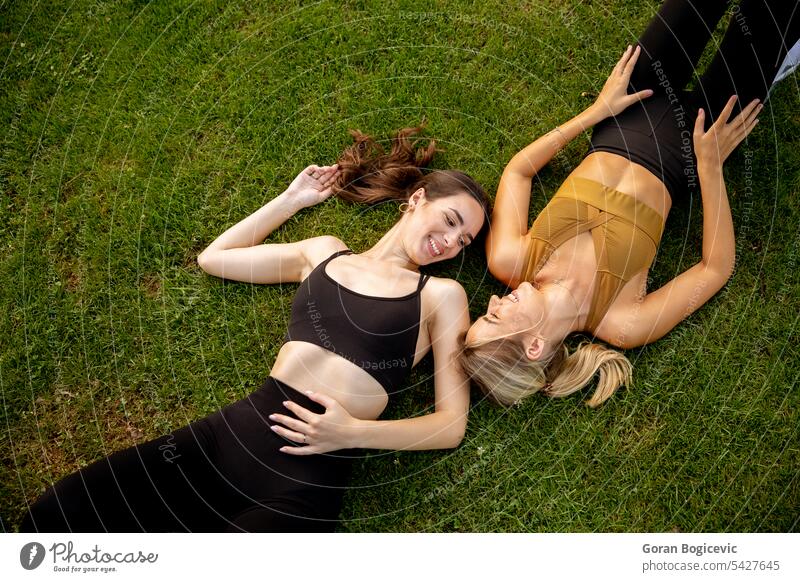 Two pretty young women laying on grass friendship caucasian two female people face adult couple cute hair casual park together green portrait fun woman beauty