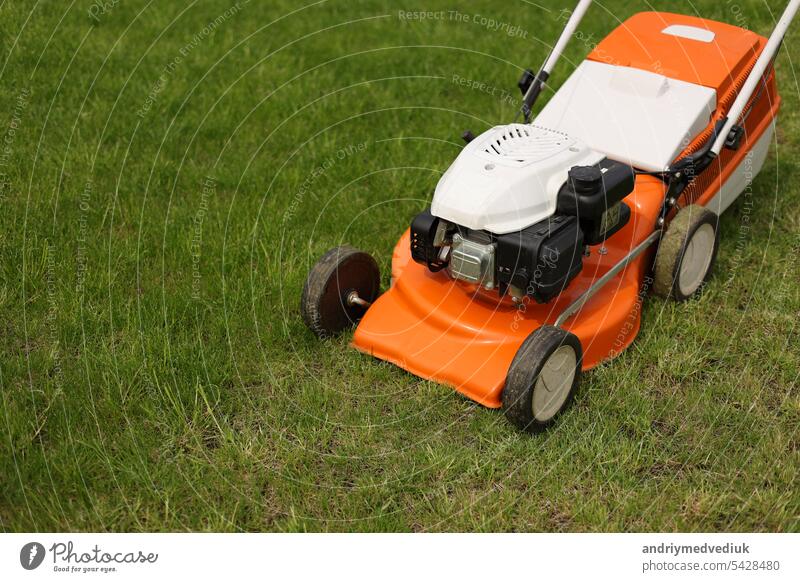 Top view of modern orange-grey electric lawn mower cutting bright lush green grass. Gardening work tools. Rotary lawn mower machine on lawn. Professional lawn care service. Place for text