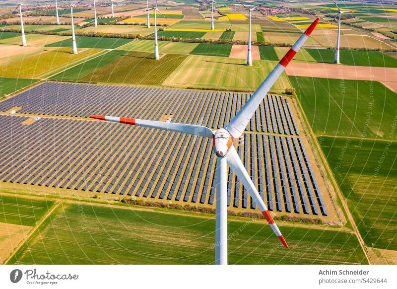 Aerial view of a wind turbine in front of agricultural fields and PV panels of a solar park wind turbines agri-PV huge agricultural land rural area