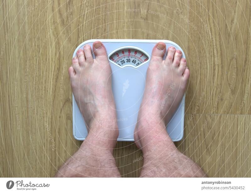 Man's feet standing on bathroom scales foot body part male man adult legs person instrument measure measurement weight obese obesity overweight underweight