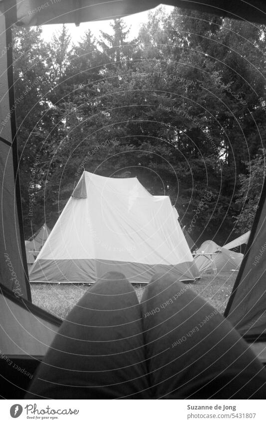 View from a tent during camping, while lying on the ground. The view is on some other tents on the camping. The image has a hazy filter, which makes the vibe chill and authentic.