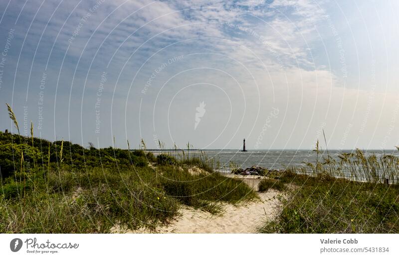 Beach pathway with lighthouse in background beach dunes ocean blue sky clouds summer beach vacation