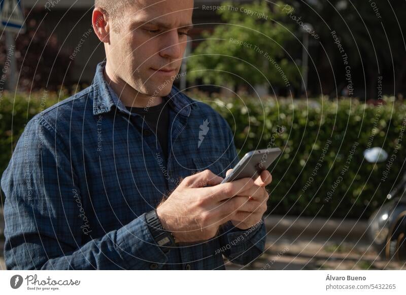A middle-aged Caucasian man, looks at his smartphone to consult some information, on the street, on a sunny day men person technology handsome male adult mobile