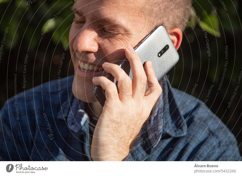 A man, chatting animatedly and smilingly on a cell phone in the street on a sunny day male mobile person adult caucasian talk young call guy lifestyles