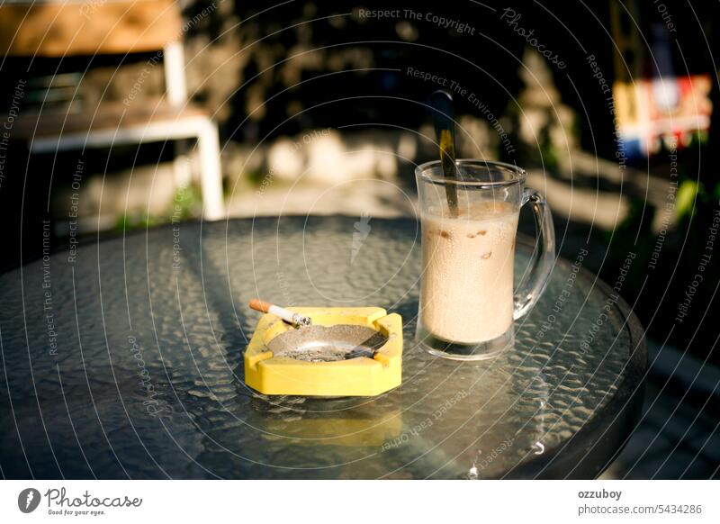 iced coffee and cigarette in yellow ashtray at sunny day drink beverage glass brown caffeine background table closeup cold food sweet smoke morning cafe fresh