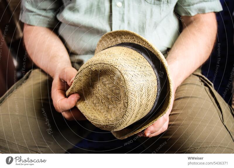 A summer dressed man holds his bright straw hat in his hands Hat summer hat Straw hat Summer Sit Man Gentleman Holiday season Headwear Sun ardor Hot Light