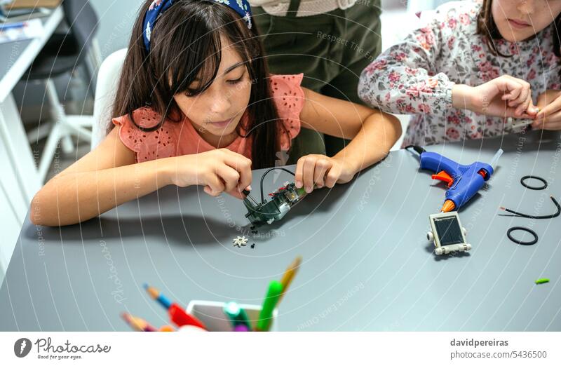Student screwing electrical circuit next to her teacher and to schoolchild in robotics class student children female electronic screwdriver concentrate wire