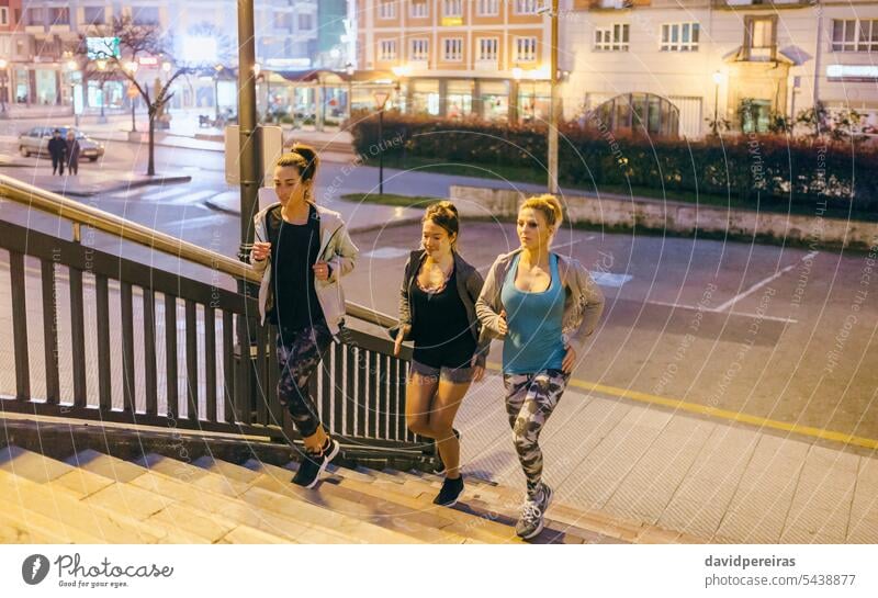 Women friends training running up stairs in city at night female team group runner women staircase step leg action speed happy together friendship sport strong