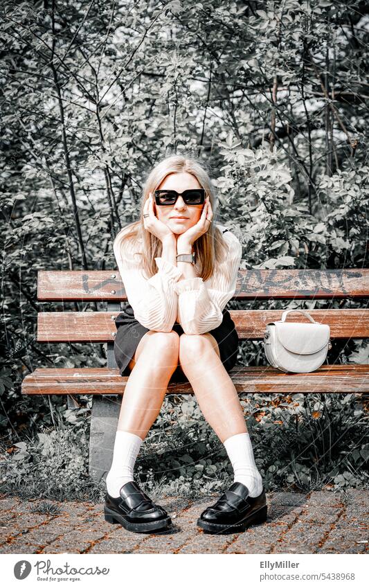 Portrait of young blonde woman with sunglasses sitting on a bench in the park. Woman youthful portrait Long-haired Feminine feminine Face naturally long hairs