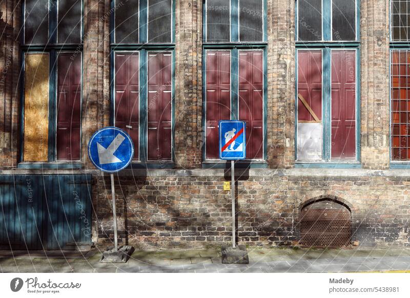 Blue traffic signs in the sunshine in front of an old brick facade with old windows in the alleys of the old town of Bruges in West Flanders in Belgium