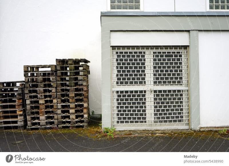 Stacked wooden euro pallets in front of a white building with a barred door on the yard of a winegrower in Traben-Trarbach on the Moselle river in the district of Bernkastel-Wittlich in Rhineland-Palatinate, Germany