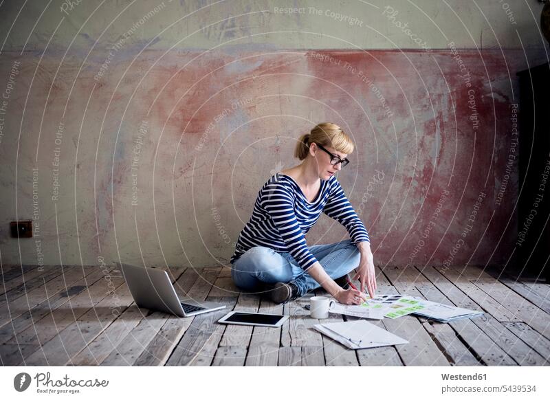 Woman sitting on wooden floor in an unrenovated room of a loft working woman females women lofts Adults grown-ups grownups adult people persons human being