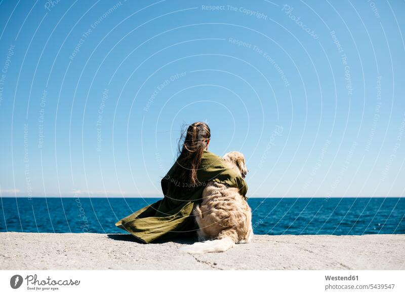 Back view of woman sitting besides her Labrador Retriever at quay looking at horizon Barcelona downshifting Slow Movement Simple Living Downshifting simple life
