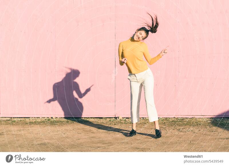 Happy young woman dancing in front of a pink wall happiness happy walls Rosy females women colour colours Adults grown-ups grownups adult people persons