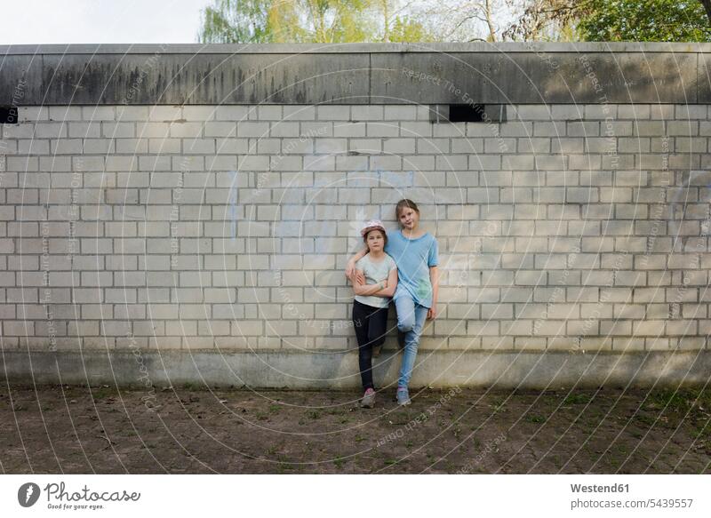 Portrait of two girls standing at a brick wall friends mate female friend T- Shirt t-shirts tee-shirt embrace Embracement hug hugging free time leisure time