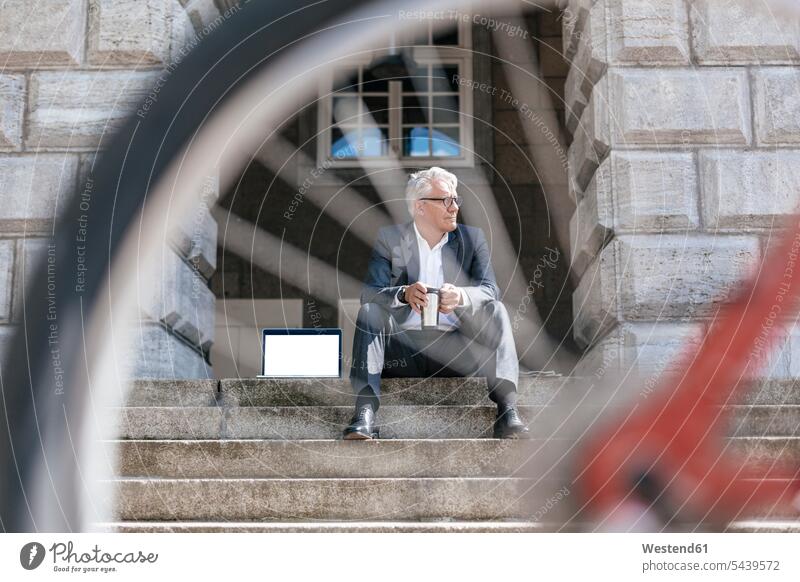 Senior businessman with bicycle sitting on stairs outdoors with laptop and travel mug Laptop Computers laptops notebook Businessman Business man Businessmen