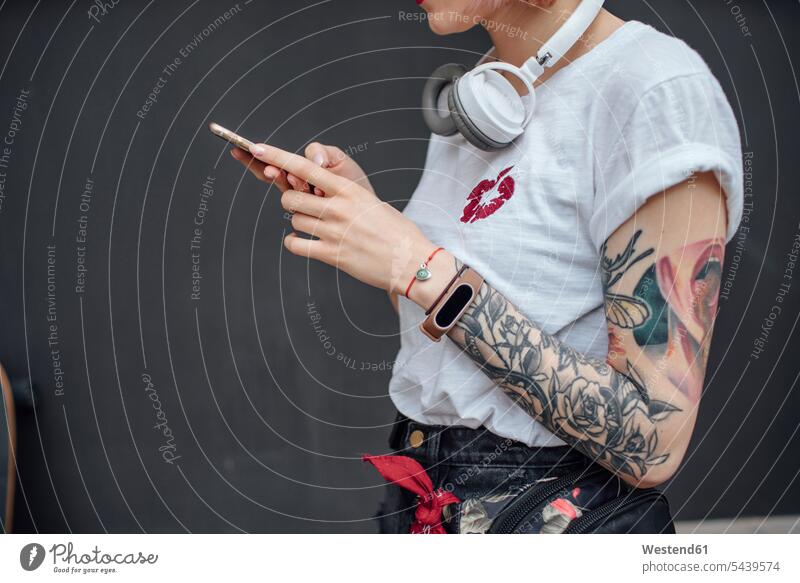 Close-up of tattooed young woman with headphones using cell phone headset cool attitude composed coolness laid-back females women mobile phone mobiles